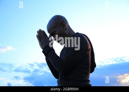 Mann, der mit den Händen zu gott betet Karibischer Mann, der mit einem Stockfoto im Hintergrund betet Stockfoto