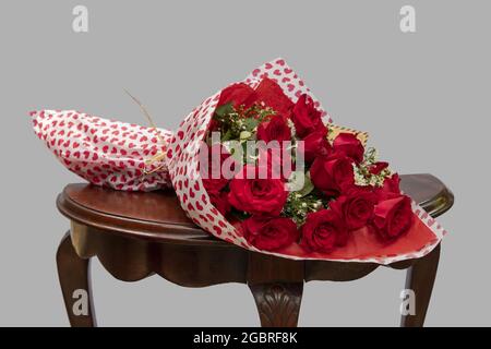 Strauß frischer roter Rosen auf einem Holzhocker auf grauem Hintergrund Stockfoto