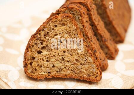 Frisches schwarzes Brot mit Sonnenblumenkernen, Leinsamen und Kürbiskernen, die auf einem Holzhintergrund in Stücke geschnitten wurden. Gesundes Lifestyle-Konzept. Stockfoto