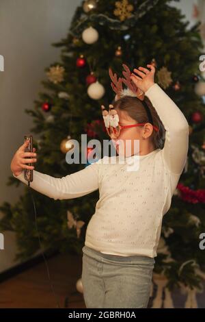 Weihnachtskonzept - Mädchen mit lustigen Weihnachtsmann Brille macht Selfie Foto in der Nähe dekorierten Weihnachtsbaum. Frohes neues Jahr. Stockfoto