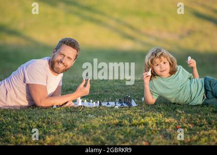 Glückliche Familie von Vater Mann und Sohn Kind spielen Schach auf grünem Gras im Park im Freien, Freundschaft Stockfoto