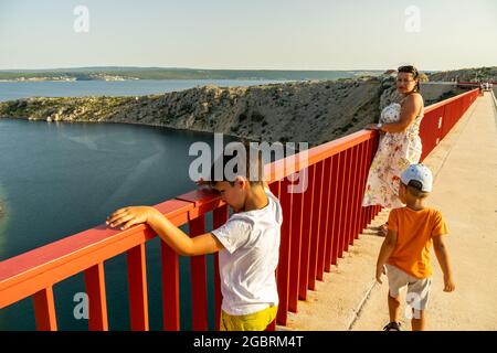 ZADAR, KROATIEN - 10. Jul 2021: Eine Frau mit ihren Kindern auf einer langen Brücke über den Fluss Zrmanja in Zadar, Kroatien Stockfoto