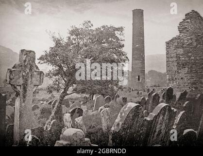 Ein Blick aus dem späten 19. Jahrhundert auf den runden Turm in Glendalough, einem Gletschertal in der Grafschaft Wicklow, Irland, bekannt für eine frühmittelalterliche Klostersiedlung, die im 6. Jahrhundert von St. Kevin, einem Nachkommen einer der regierenden Familien in Leinster, gegründet wurde. Der runde Turm ist etwa 30 Meter hoch, mit einem Eingang 3.5 Meter vom Sockel entfernt, und hätte sechs Holzböden gehabt, die durch Leitern verbunden waren. Die vier Stockwerke über der Eingangsebene werden jeweils durch ein kleines Fenster beleuchtet, während das oberste Stockwerk vier Fenster hat, die auf die Himmelsrichtungen zeigen. Es diente seberalen Funktionen, Wahrzeichen für den bevorstehenden Besuch Stockfoto