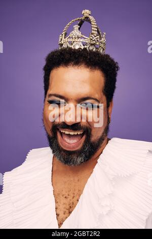 Fröhlicher Mann mit Bart trägt Make-up und ziehen Königin Krone. Bärtiger Mann trägt Krone und Make-up lachen. Stockfoto