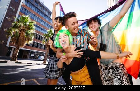 Junge Menschen, die sich nicht an das Geschlecht halten und den Stolz der Homosexuellen feiern. Eine Gruppe glücklicher queerer Menschen, die fröhlich lächeln, während sie eine Regenbogenflagge aufwerfen. Memb Stockfoto