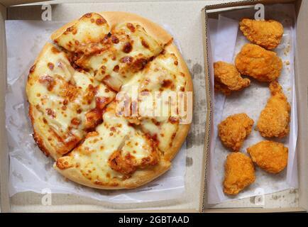 Draufsicht auf Pizza in brauner Papierkiste und gebratenes Huhn, ein Junk-Food-Lunch-Set. Stockfoto