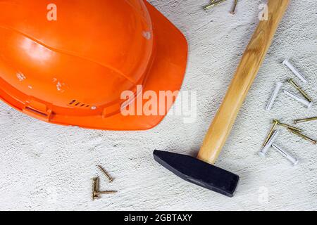 Oranger Schutzhelm mit Klauenhammer auf hellgrauem Zementhintergrund. Hausreparatur und Verbesserung, Hausbau Konzept. Stockfoto