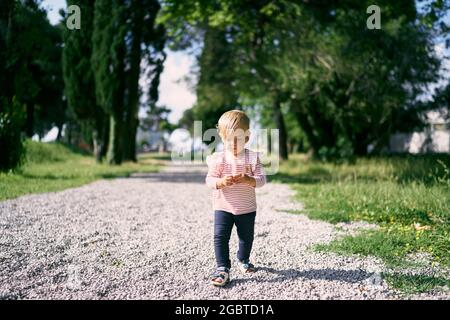 Kleines Mädchen, das auf einem Kiesweg in einem grünen Park läuft Stockfoto