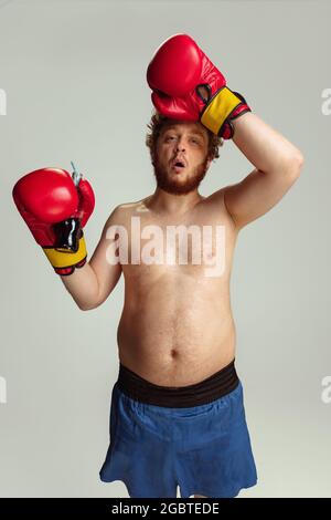 Lustiger rotköpfiger Mann in blauen Boxshorts und Handschuhen isoliert auf grauem Studiohintergrund. Konzept von Sport, Humor und Körper positiv. Stockfoto