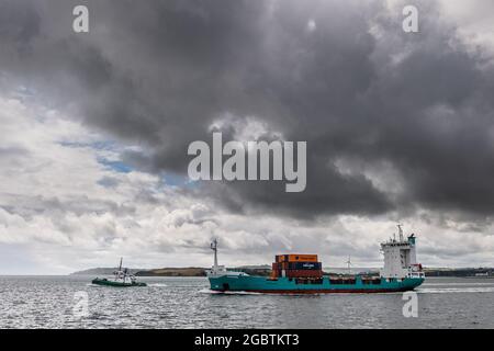 Cobh, County Cork, Irland. August 2021. Met Éireann hat eine gelbe Wetterwarnung für Starkregen und Gewitter herausgegeben, die zu örtlich begrenzten Überschwemmungen und gefährlichen Fahrbedingungen führen wird. Die Warnung ist bis zum 22.00. September heute Abend in Kraft. Das Containerschiff „Ragna“ segelt unter einer bedrohlichen schwarzen Wolke, als sie den Hafen von Cork verlässt, begleitet vom Schlepper „DSG Titan“. Quelle: AG News/Alamy Live News Stockfoto