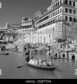 In den 1950er Jahren, geschichtlich, drängten sich Menschen in einem kleinen hölzernen Ruderboot auf dem Ganges-Fluss, Bernares, Indien. Der Fluss zieht Tausende von Pilgern zum Baden an seine Ufer, da sie als heilige Gewässer gelten. Stockfoto
