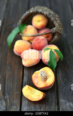 Nahaufnahme von frischen, saftig reifen Pfirsichen, die neben einem Korbkorb auf einem alten Holztisch verstreut sind, selektiver Fokus am unteren Bildrende. Gesunde Ernährung Stockfoto