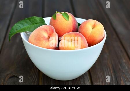 Weiße Schale mit reifen Pfirsichfrüchten auf einem rustikalen Holztisch. Gesunde Ernährung Konzept. Stockfoto