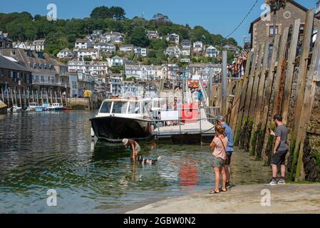 Looe, Cornwall, England, Großbritannien. 2021. Urlauber, die eine Bootsfahrt besteigen und eine Frau mit ihrem Hund im Hafen bei ankommender Flut. Stockfoto