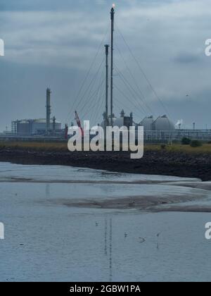 Mitten im Industriekomplex von North Tees leuchtet ein Fackel, während Möwen über das Watt schweben, ein Glanz von Wasser spiegelt die Szene wider. Stockfoto