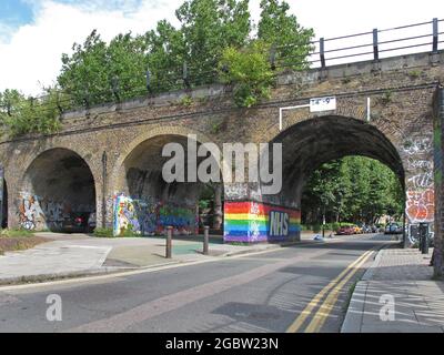 Das viktorianische Backsteinviadukt kreuzt Creekside, eine Straße in Deptford, im Südosten Londons, Großbritannien. Überwuchert, immer noch in Gebrauch, zeigt NHS-Regenbogengraffiti. Stockfoto