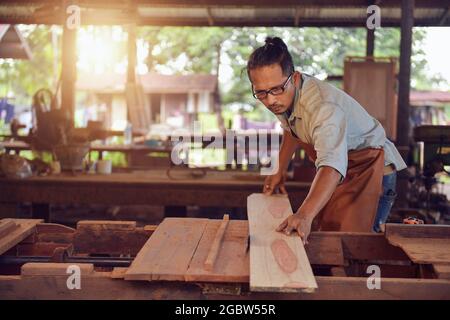Gelernter Zimmermann, der in seiner Holzwerkstatt ein Stück Holz schneidet, Tischler, die in der Werkstatt eine Kreissäge verwenden, im Vintage-Stil Stockfoto