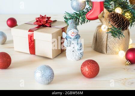 Weihnachtsbaumschmuck auf dem Tisch. Konzept für die Urlaubsvorbereitung. Kleiner Spielzeug-Schneemann, Geschenkbox und rote Kugeln. Stockfoto