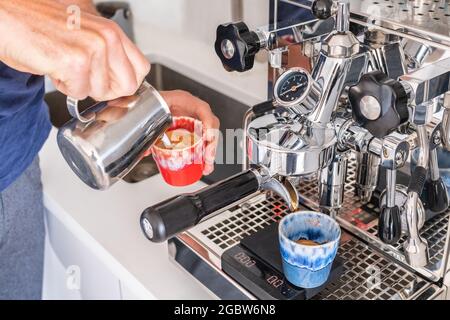 Barista macht Cortado an der Kaffeemaschine und gießt Milch in die Espressotasse im Café. Home Morgen trinken Frühstück in der Küche Stockfoto