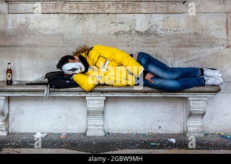Ein junger Mann schläft auf EINER Bank auf dem Markusplatz während des Karnevals in Venedig, Italien. Stockfoto