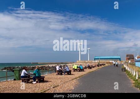 Southwick Promenade in der Nähe von zwei Windturbinen mit Menschen, die draußen sitzen und die Sommersonne genießen. Stockfoto