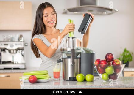 Grüne Saft Frau entsaften Sellerie und Apfelsaft mit Entsafter Maschine zu Hause. Hausgemachter frischer Gemüsesaft diy in der Küche. Glückliche asiatische Mädchen Stockfoto