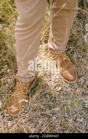 Beine des Bräutigams in braunen Hosen auf dem gelben trockenen Gras. Nahaufnahme Stockfoto