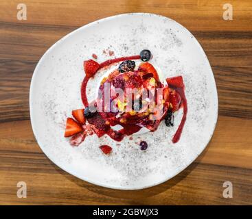 Gourmet-Erdbeer-Pavlova-Kuchen mit frischen Beeren und Schichten von Schlagsahne und Baiser auf einem Teller serviert, Stockfoto