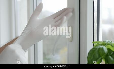 Hand mit Schutzhandschuh öffnet ein Fenster in einem Krankenhauszimmer Stockfoto