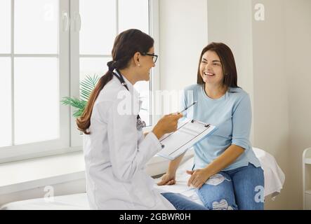 Fröhlicher junger Arzt und Patient, die während der Untersuchung im Krankenhaus reden und lachen Stockfoto