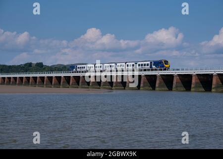 Ein Zug fährt über die Brücke, die die Mündung des Flusses Kent überspannt, während er in Arnside, Lancashire, England, ins Meer mündet. Stockfoto