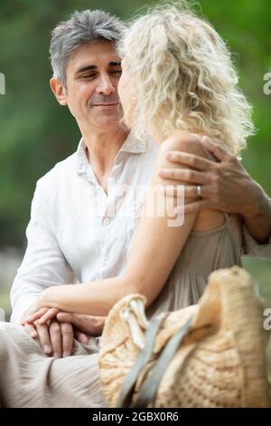 Ein älterer Mann umarmt seine Frau, die auf der Bank steht Stockfoto