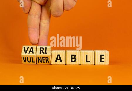 Verletzlich oder variables Symbol. Geschäftsmann dreht Holzwürfel und ändert das Wort anfällig für variable. Schöner orangefarbener Hintergrund, Kopierbereich. Bu Stockfoto