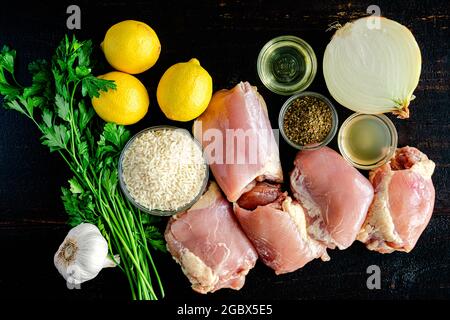 Griechisches Huhn und Zitronenreis Zutaten auf einem Holzhintergrund: Rohe Hühnerschenkel, Langkornreis, Zitronen und andere Zutaten auf einem Holztisch Stockfoto