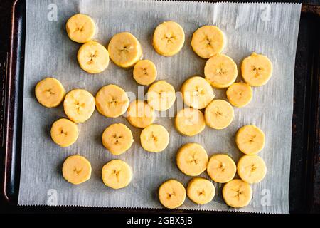 Geschnittene Kochbananen auf einem mit Pergament überzogenen Blech Pfanne: Scheiben roher Kochbananen auf einem Backblech Stockfoto