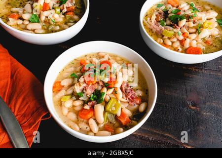 Schüsseln weiße Bohnen- und Schinken-Suppe mit Brot: Drei Schüsseln Cannellini-Bohnensuppe mit geräuchertem Schweinefleisch und Gemüse Stockfoto