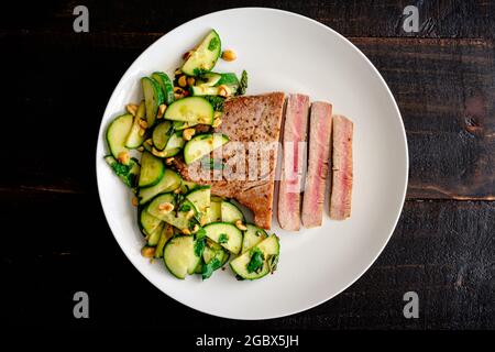 Thunfischsteak mit Gurken-Erdnusssalat: Seltenes Fischfilet, serviert mit Gurken- und Erdnusssalat als Beilage Stockfoto