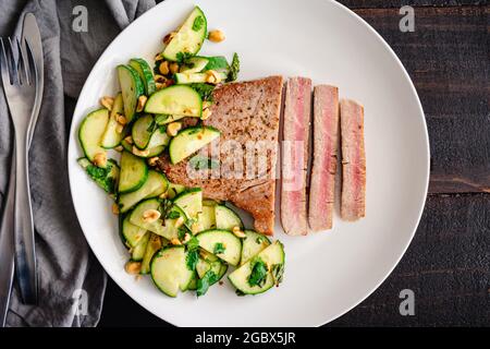 Thunfischsteak mit Gurken-Erdnusssalat: Seltenes Fischfilet, serviert mit Gurken- und Erdnusssalat als Beilage Stockfoto