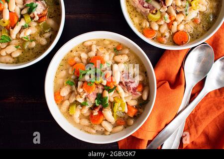 Schüsseln weiße Bohnen- und Schinken-Suppe mit Brot: Drei Schüsseln Cannellini-Bohnensuppe mit geräuchertem Schweinefleisch und Gemüse Stockfoto