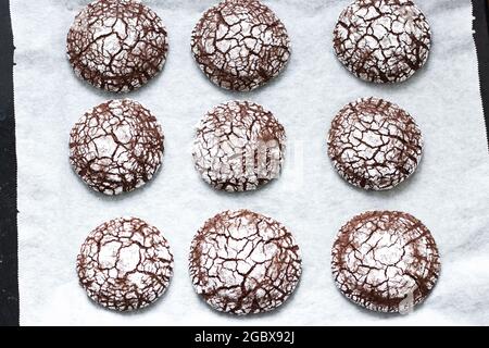 Hausgemachte Schokolade crinkle Cookies in Pulverzucker auf einem Pergamentpapier. Hintergrund der Speisen. High-Angle-Ansicht. Stockfoto
