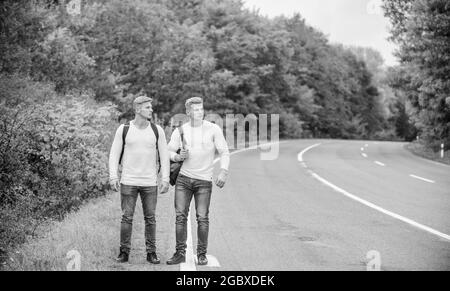 Muss gehen. Fernweh-Konzept. Wandern mit Freunden ist cool. Gegangen, um sich selbst zu finden. Reisen Sie mit dem Kraftheber. Zwillinge wandern entlang der Straße. Kraftheber wandern weiter Stockfoto