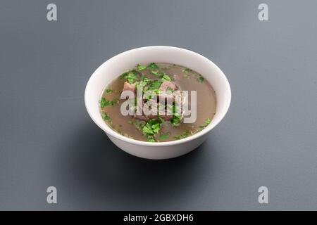 Nahaufnahme der Knochenbrühe mit Rindfleisch und Petersilie in einer Schüssel auf grauem Hintergrund Stockfoto