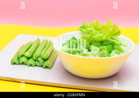 Frisch gehackte Sellerie-Scheiben in weißer Schüssel mit Sellerie-Sticks auf weißem Schneidebron. Vegane und vegetarische Kultur. Rohkost. Gesunde Ernährung mit negativem Kaloriengehalt Stockfoto