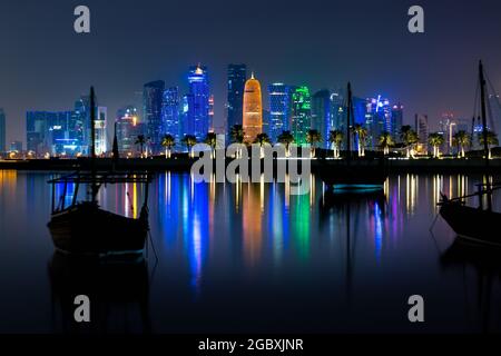 Doha, Katar - 29. September 2019: Kolofulige beleuchtete Skyline von Doha bei Nacht mit traditionellen Holzbooten namens Daus im Vordergrund, Katar, Mi Stockfoto