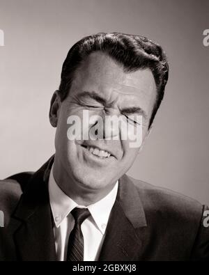 1950S 1960S BUSINESS MAN BLINZELN AUGEN GESCHLOSSEN LUSTIG GESICHTSAUSDRUCK VERÄRGERT ÜBER ZU NIESEN - P7024 HAR001 HARS PERSONEN MÄNNER RISIKO B&W FRUSTRIERT BIZARRE BRÜNETTE KOMISCHE KOPF UND SCHULTERN ENTDECKUNG SORRY GROTESKE SCHIELENDE ZANY UNKONVENTIONELLE FRUSTRATION POLITIK TEMPERAMENT BESCHÄMT KONZEPTUELL VERRÜCKTES EIGENWILLIGES BEDAUERN SCHIELT AMÜSANT EXZENTRISCH VERÄRGERT IRRITIERT MITTLEREN ERWACHSENEN MANN GRINSEN SCHWARZ UND WEISS KAUKASISCHEN ETHNIE ERRATISCHE AUGEN GESCHLOSSEN HAR001 ALTMODISCH UNVERSCHÄMT Stockfoto