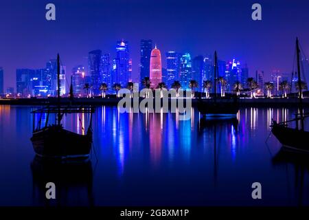 Coloful beleuchtete Skyline von Doha bei Nacht mit traditionellen Holzbooten namens Daus im Vordergrund, Katar, Naher Osten gegen dunklen Himmel Stockfoto