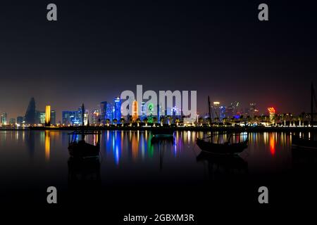 Coloful beleuchtete Skyline von Doha bei Nacht mit traditionellen Holzbooten namens Daus im Vordergrund, Katar, Naher Osten gegen dunklen Himmel Stockfoto