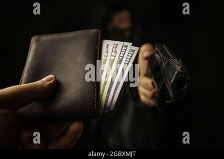 Bewaffneter Raub. Angriff auf unbewaffneten Mann. Die Hand des Mannes hält Geldbeutel aus, um sie mit der Waffe zu räubern. Hundertfünfzig Dollar in offener Geldbörse.die Schusswaffe wird auf die Kamera gerichtet. Stockfoto