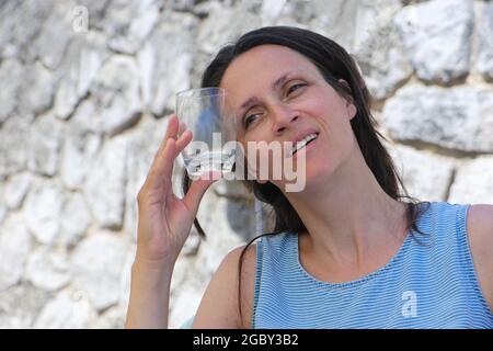Eine Frau kühlt sich ab, indem sie kaltes Trinkglas auf ihre Stirn hält. Stockfoto