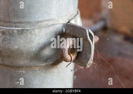 Nahaufnahme eines rostigen Metallgliedes auf einem alten Rohr in einer Fabrik mit Spinnweben überall Stockfoto